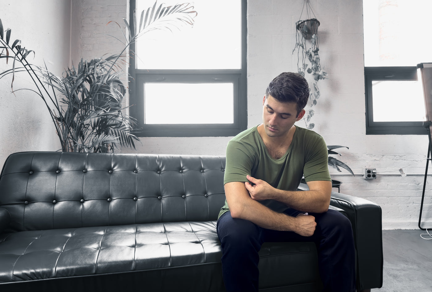 man sitting on a couch touching his forest green drop tee shirt